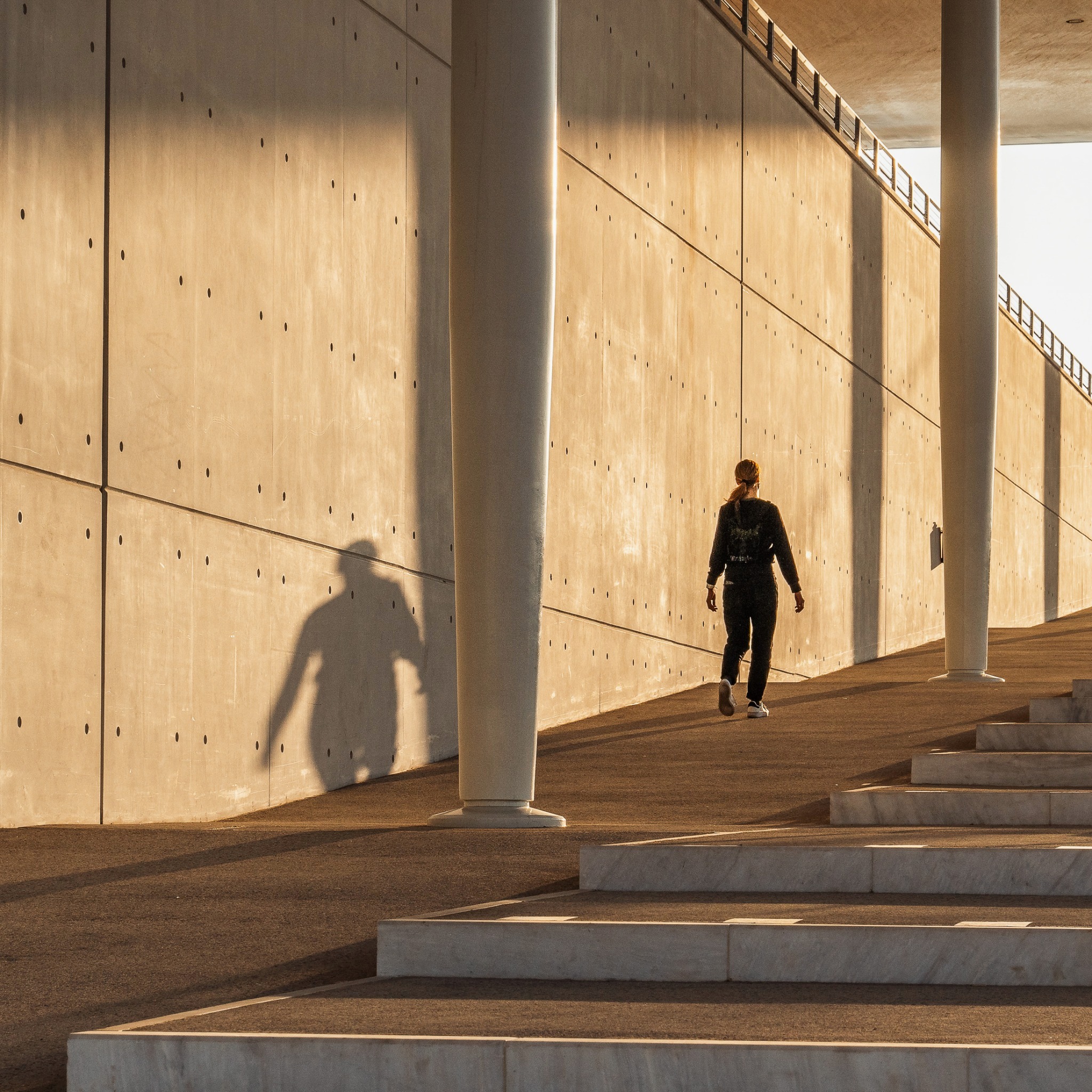 Stavros Niarchos Foundation Cultural Center — figure and shadow in a sunlit colonnade